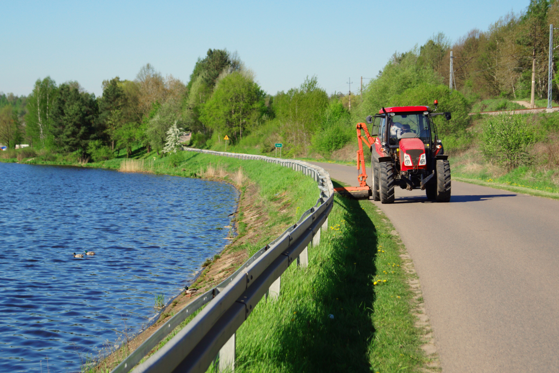 Zdjęcie traktora z&nbsp;urządzeniem koszącym przy drodze powiatowej nad Zalewem Brodzkim. Jak co roku, gmina podpisała porozumienie z&nbsp;powiatem starachowickim na&nbsp;koszenie poboczy przy drogach powiatowych o&nbsp;łącznej długości ok 66 km.&nbsp;Zadanie wykonuje Zakład Gospodarki Komunalnej w&nbsp;Brodach.